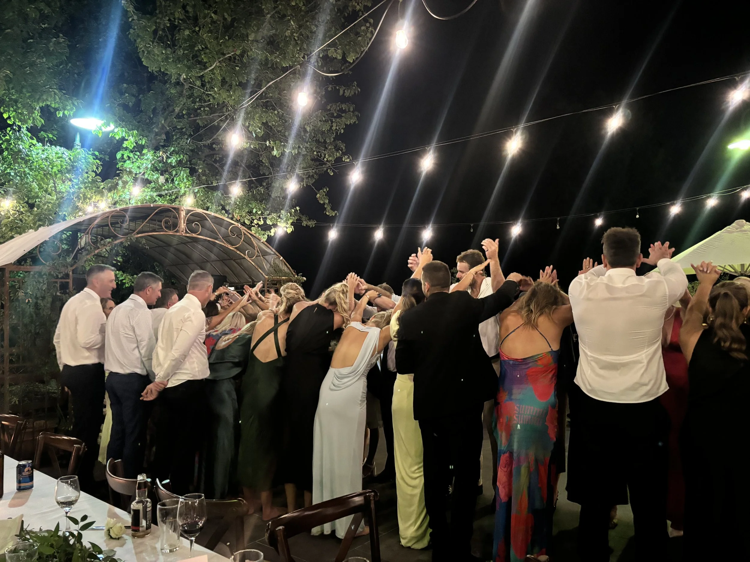 People at an outdoor celebration or party dancing under string lights at night.