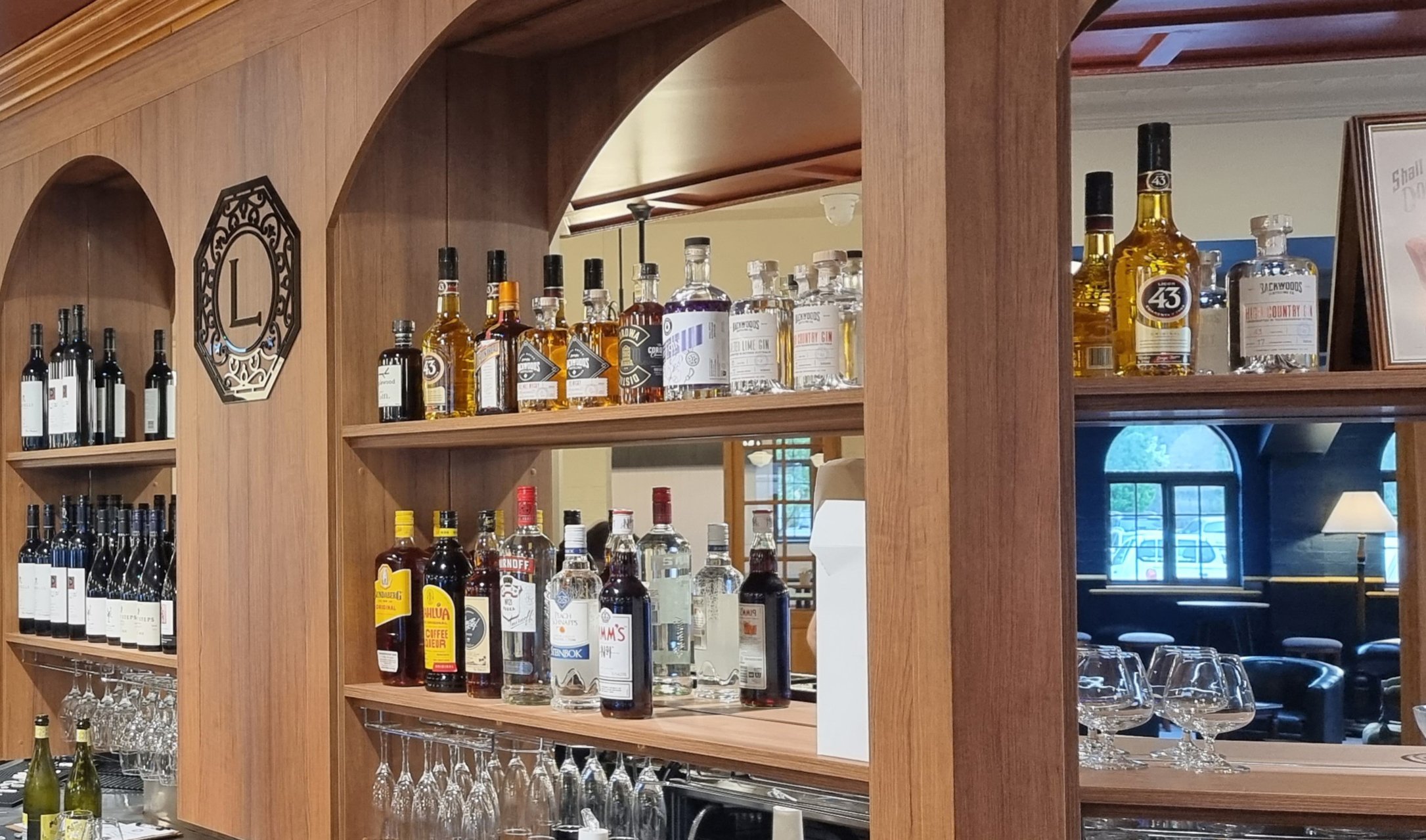 Bar shelf with various bottles of alcohol and wine glasses, visible through a wooden shelving unit.