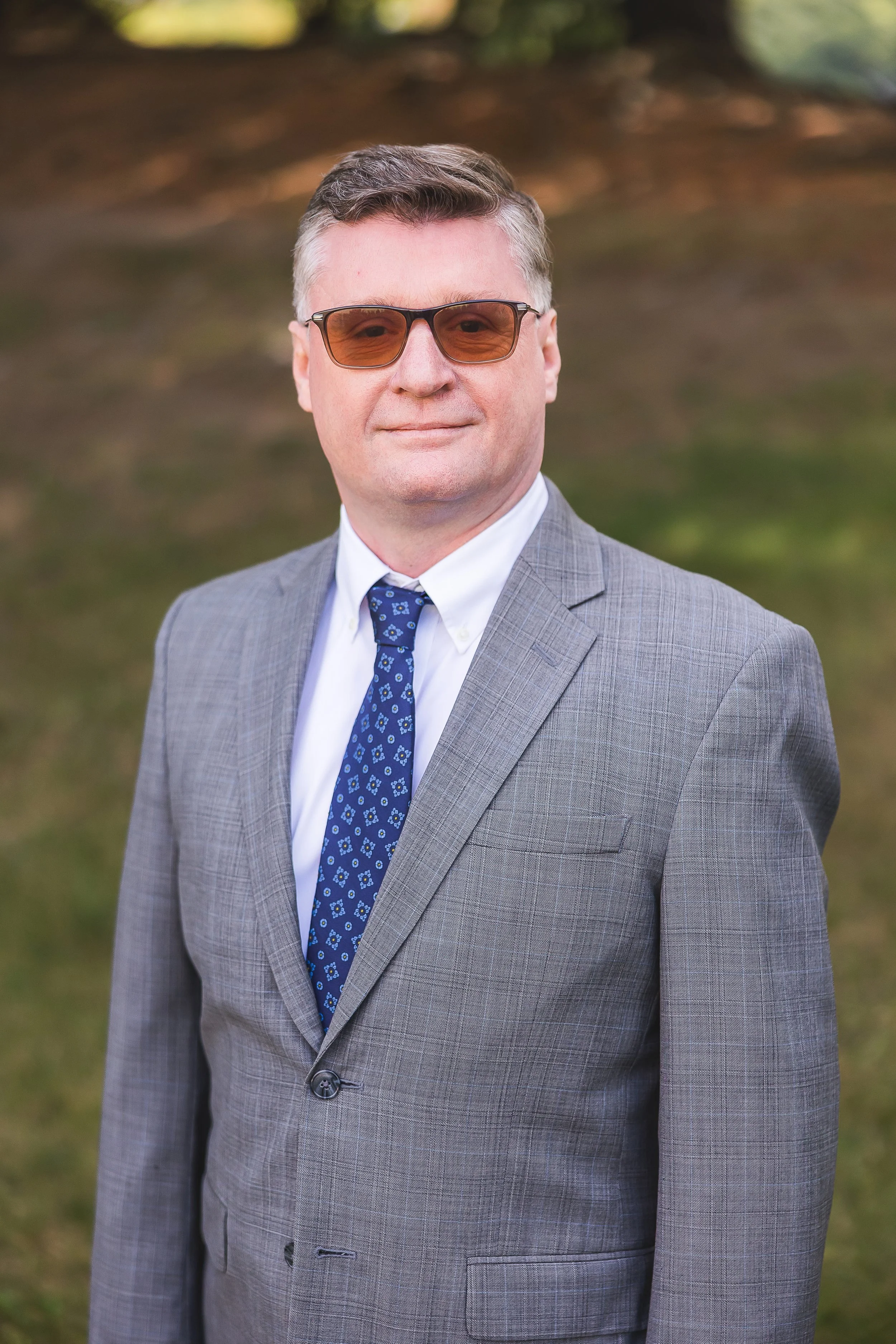 Man in a blue suit and red striped tie, wearing glasses, smiling in an office setting.