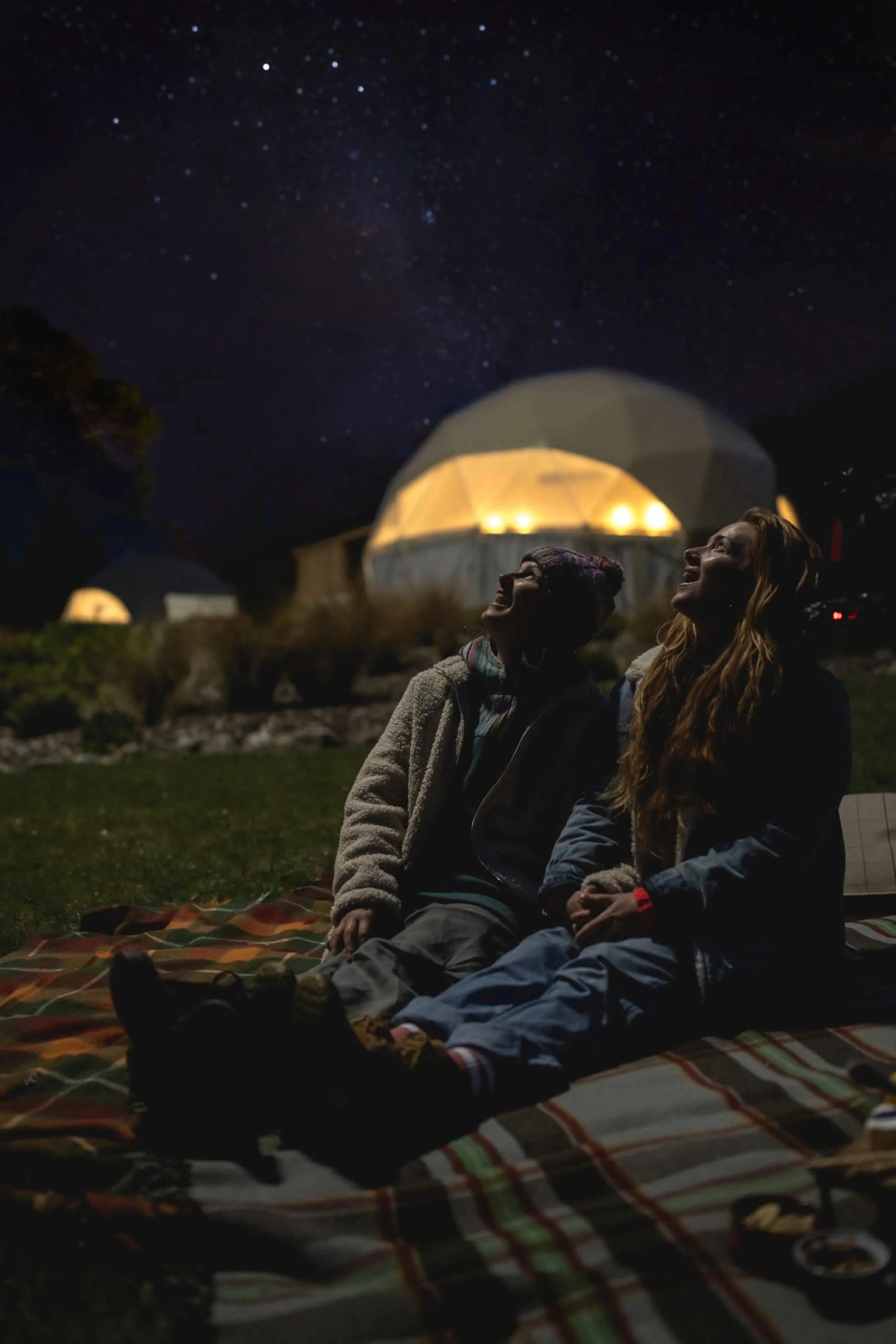 Couple stargazing beside a lit geodesic glamping dome at Lake Hawea, Otago, New Zealand