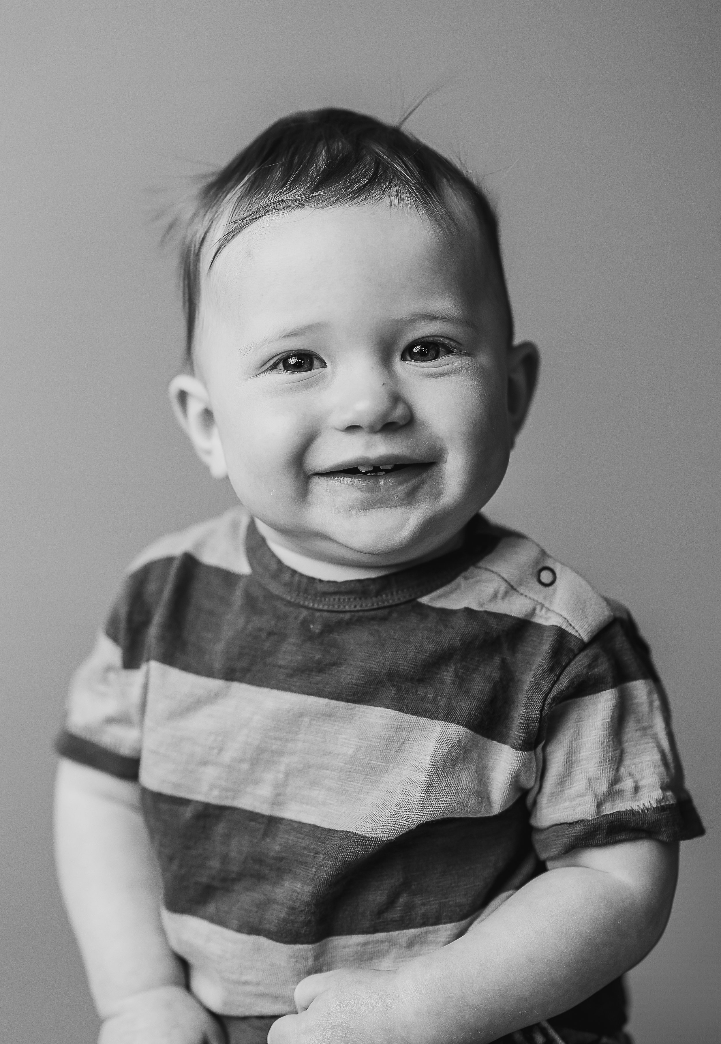 Black and white portrait of a smiling baby wearing a striped shirt.