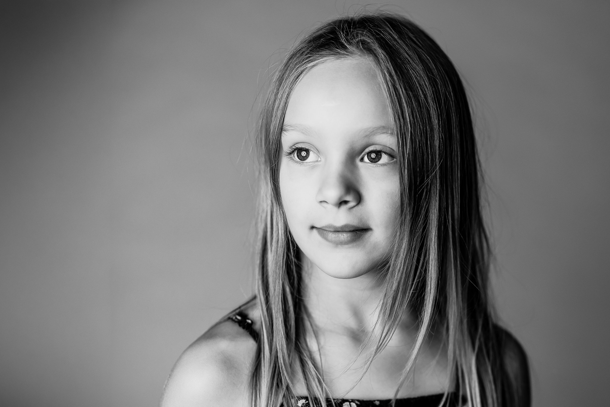 Black and white portrait of a young girl with long hair looking to the side against a gray background.