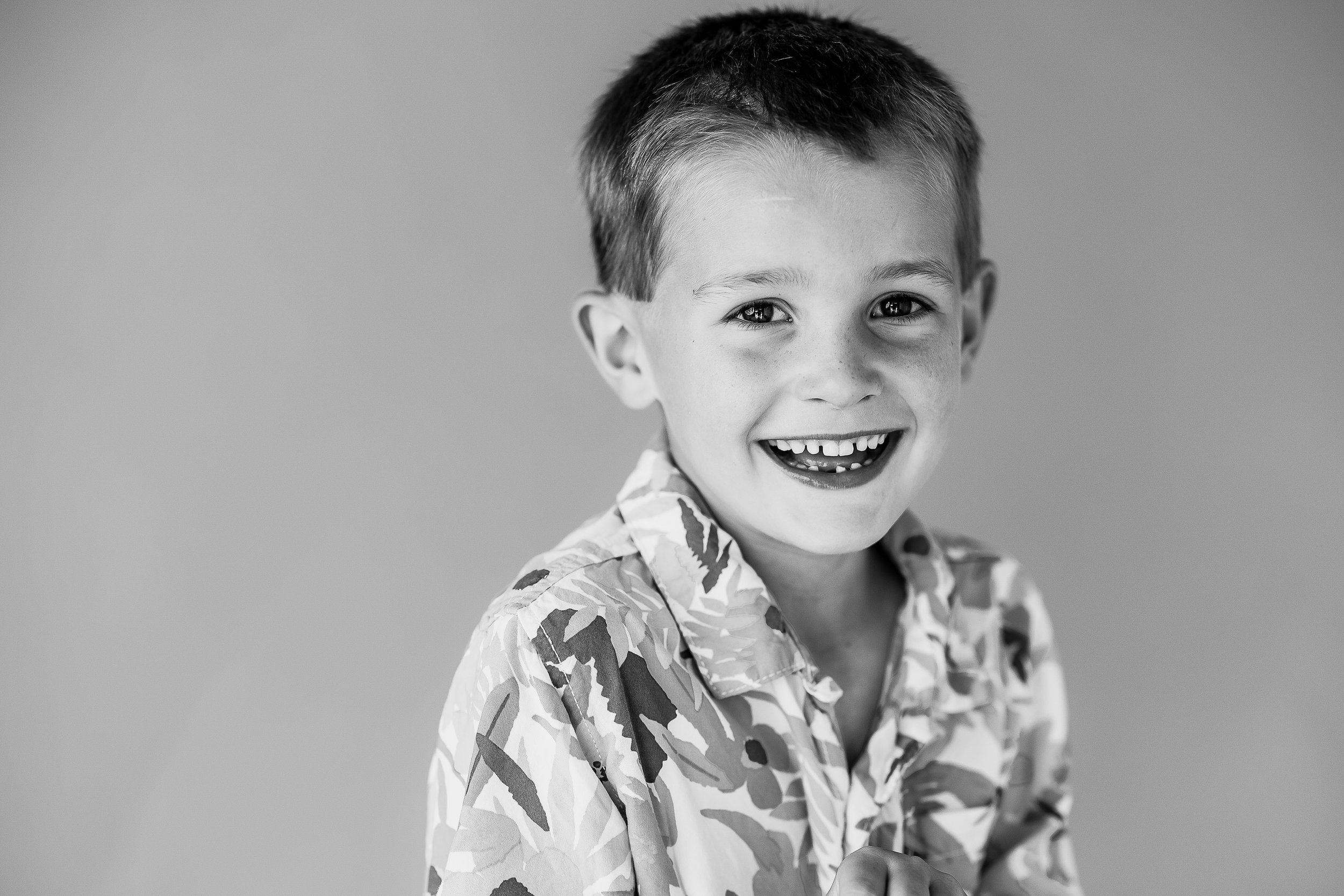 Black and white photo of a young child smiling, wearing a patterned shirt, against a plain background.
