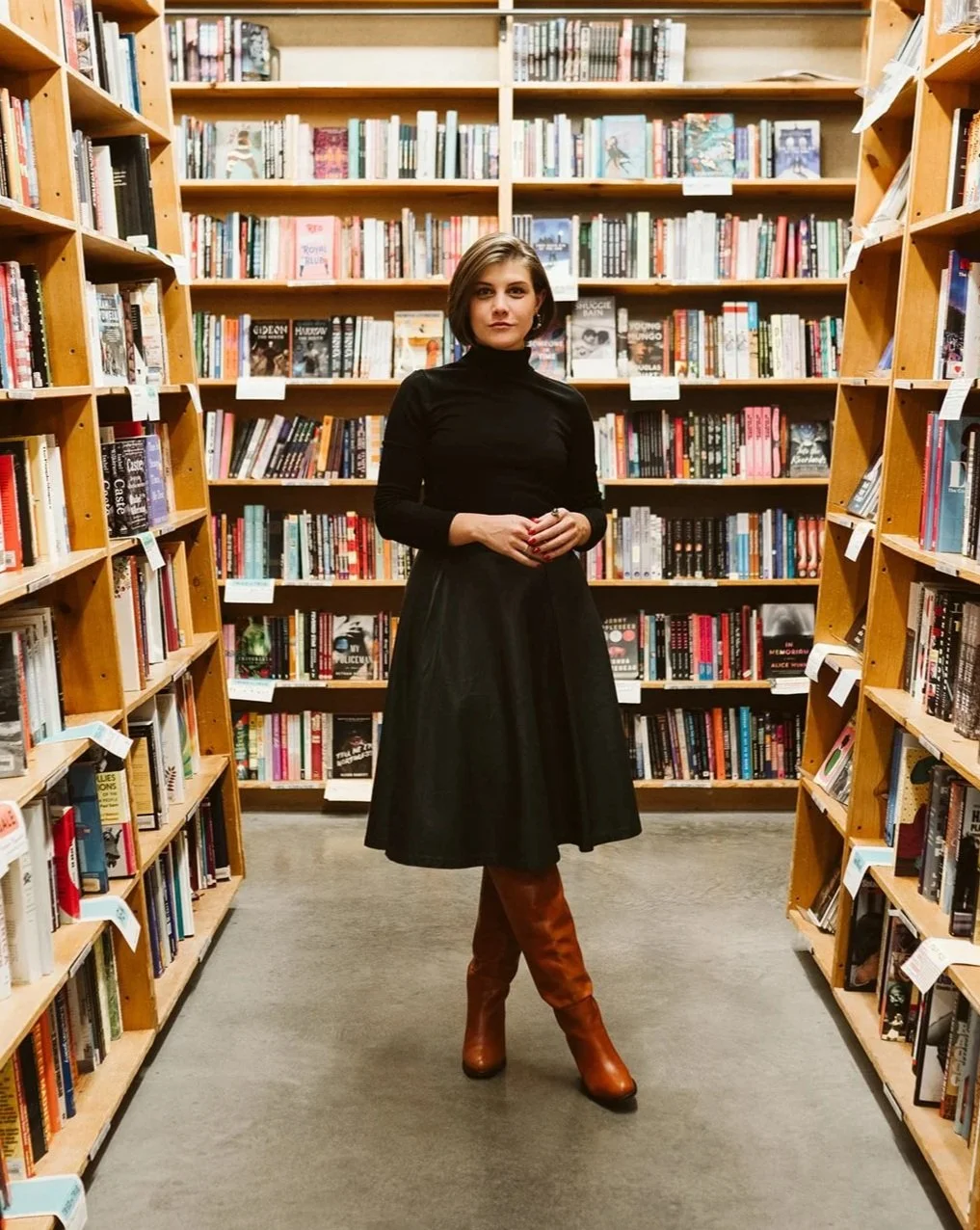 Meg stands surrounded by bookshelves, confident but relaxed.