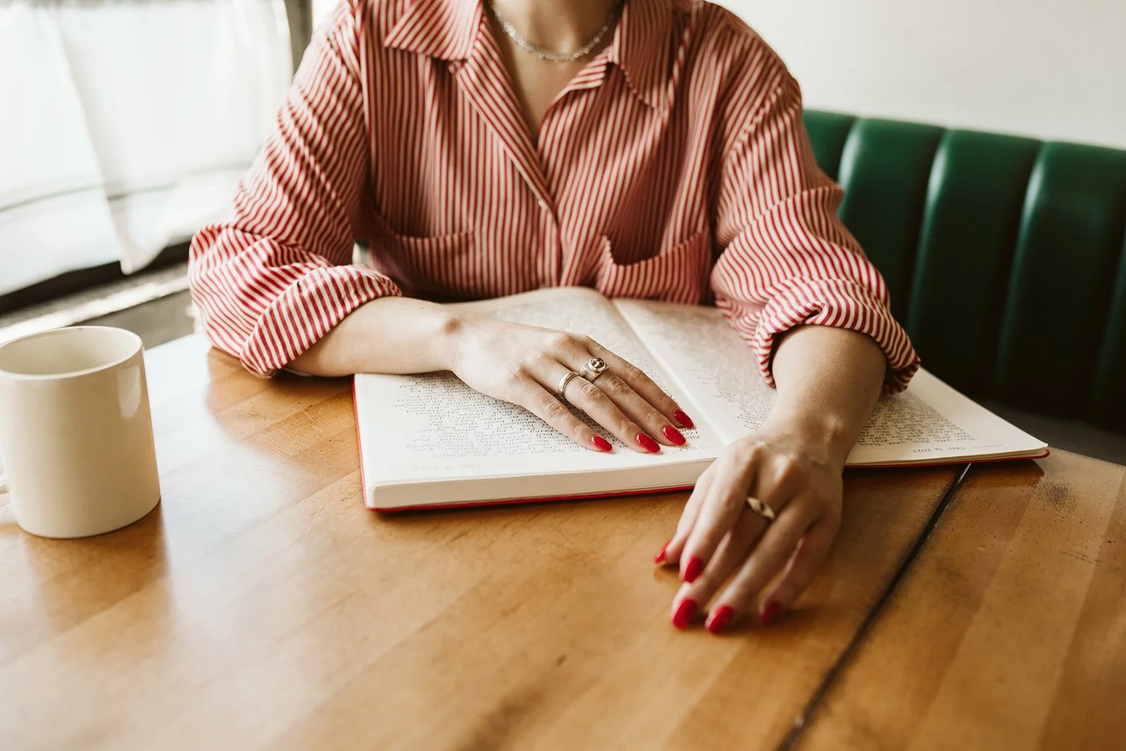Meg's hands resting on her notebook. Her long fingernails are painted red to match a red striped shirt.