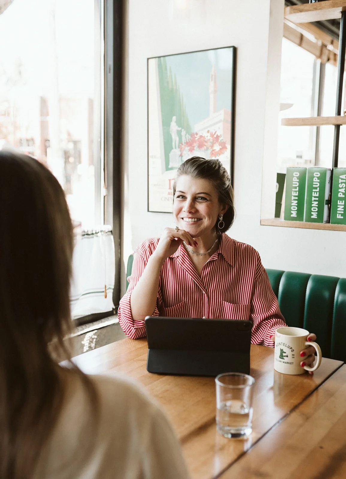 Meg smiles across a table at a client, coffee in hand and laptop open to take notes.