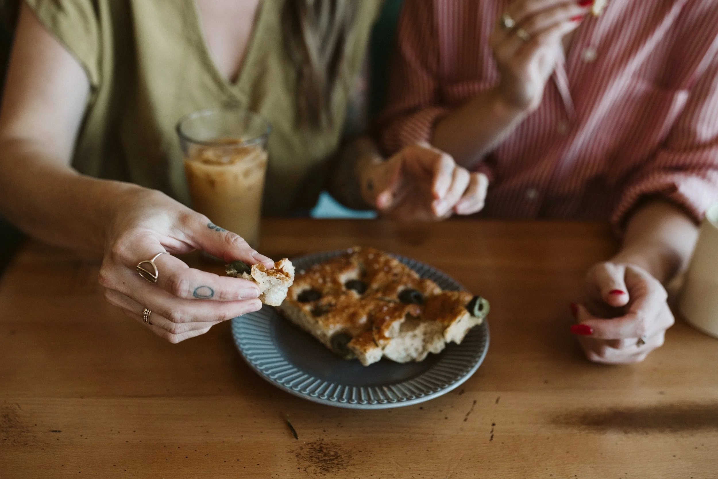 A piece of focaccia bread being shared by two tattooed hands