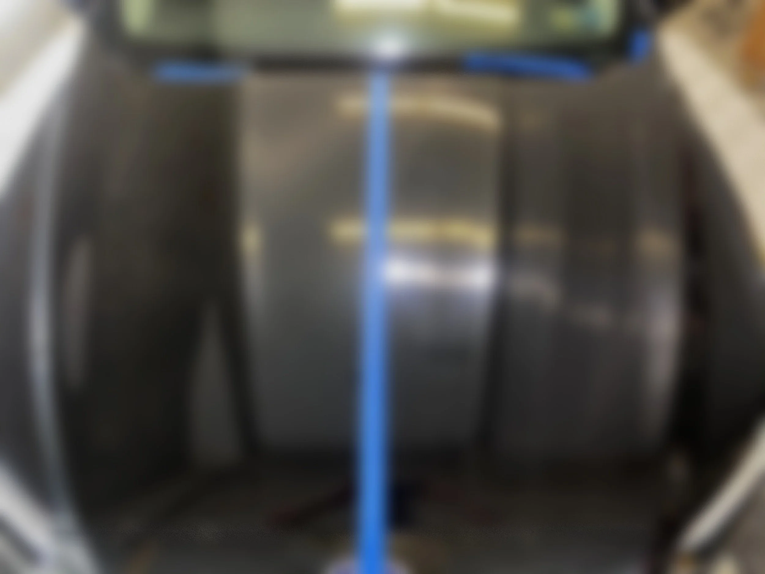 The hood of a black car with a blue painter's tape running vertically down the center, showing a freshly painted or polished surface.
