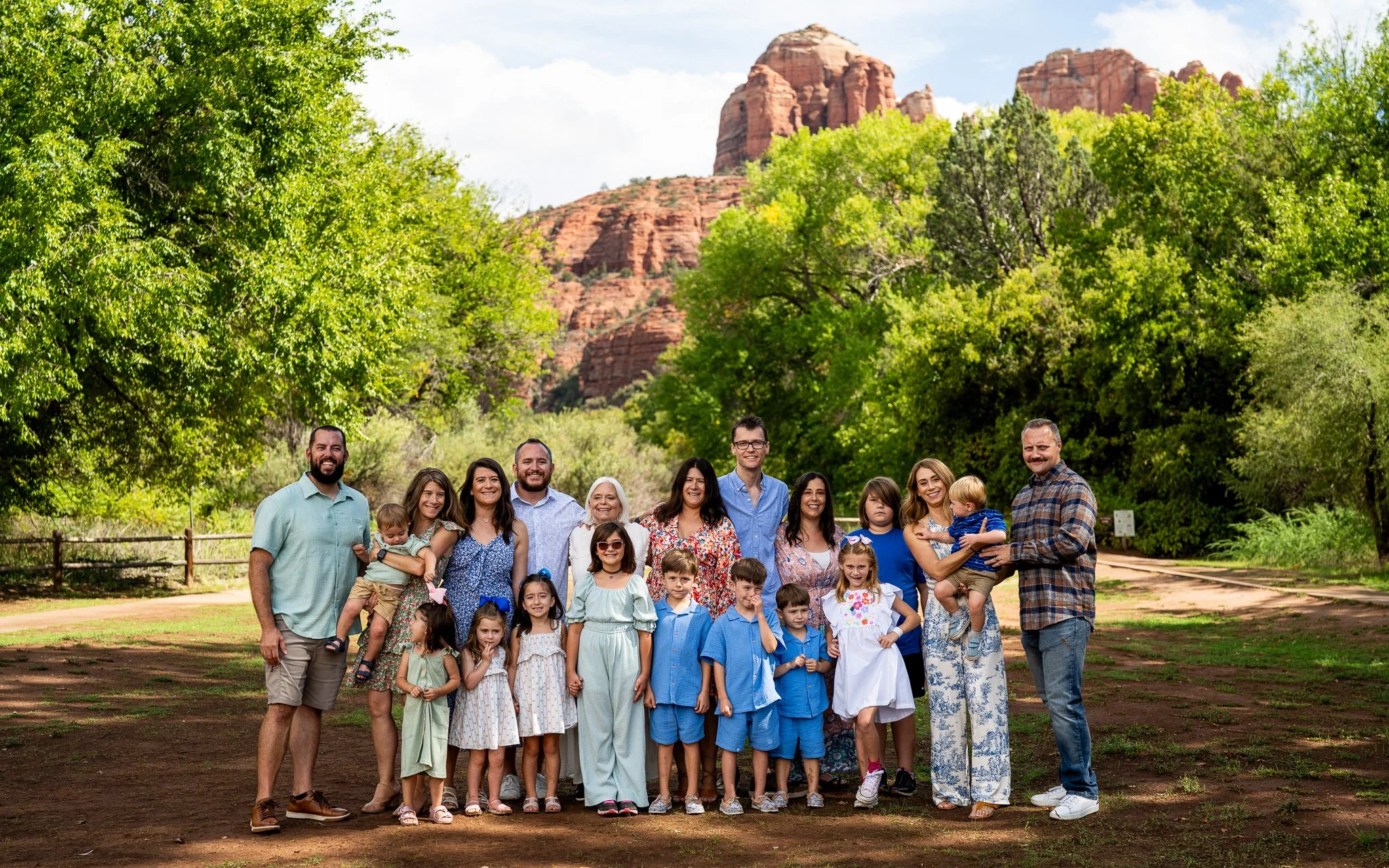 A large family gathering outdoors in front of a scenic mountain and green trees, including adults and children posing for a photo.