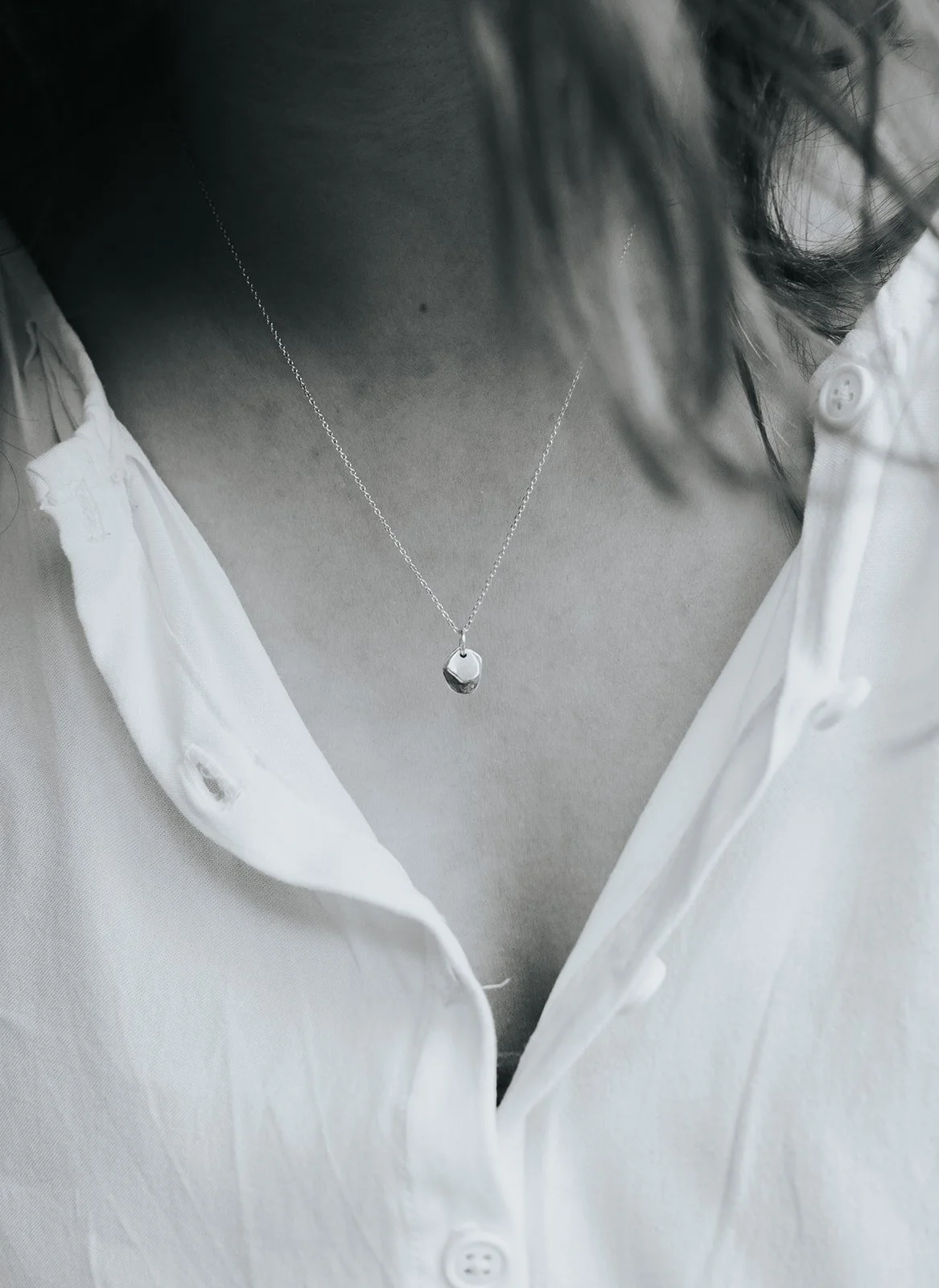 Close-up of a hand holding a necklace with a circular pendant engraved with a leaf design.