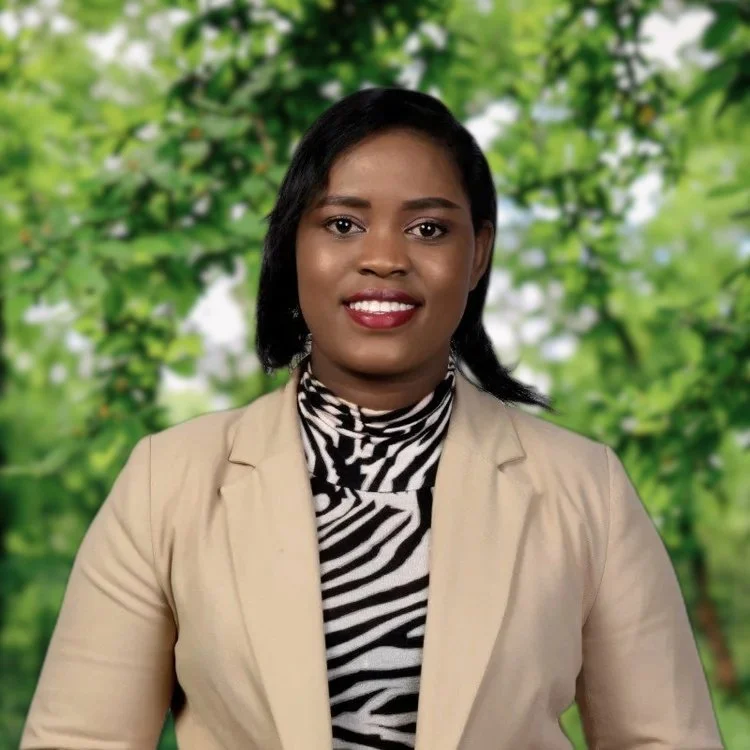 A woman with dark hair styled in a bob, wearing a beige blazer over a black and white zebra print turtleneck, smiling at the camera against a plain gray background.
