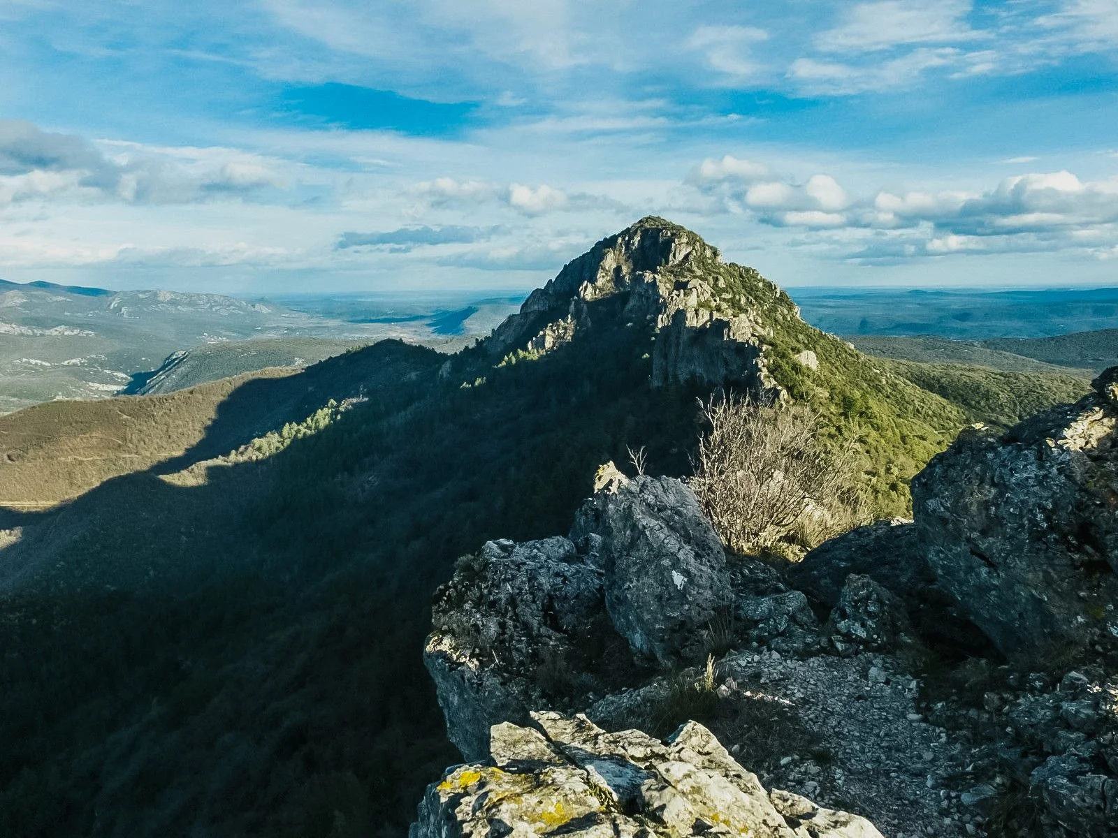 Paysage de montagnes verdoyantes avec un sommet rocheux en crete sous un ciel bleu avec quelques nuages
