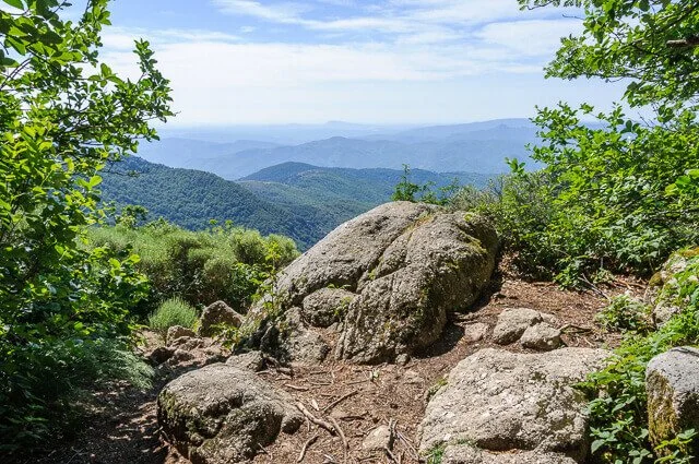 Vue sur une montagne avec des rochers et de la végétation verte, avec des montagnes en arrière-plan.