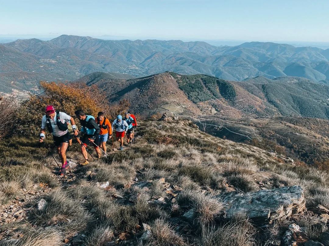 Groupe de randonneurs en marche sur un sentier de montagne avec un paysage vallonné en arrière-plan.