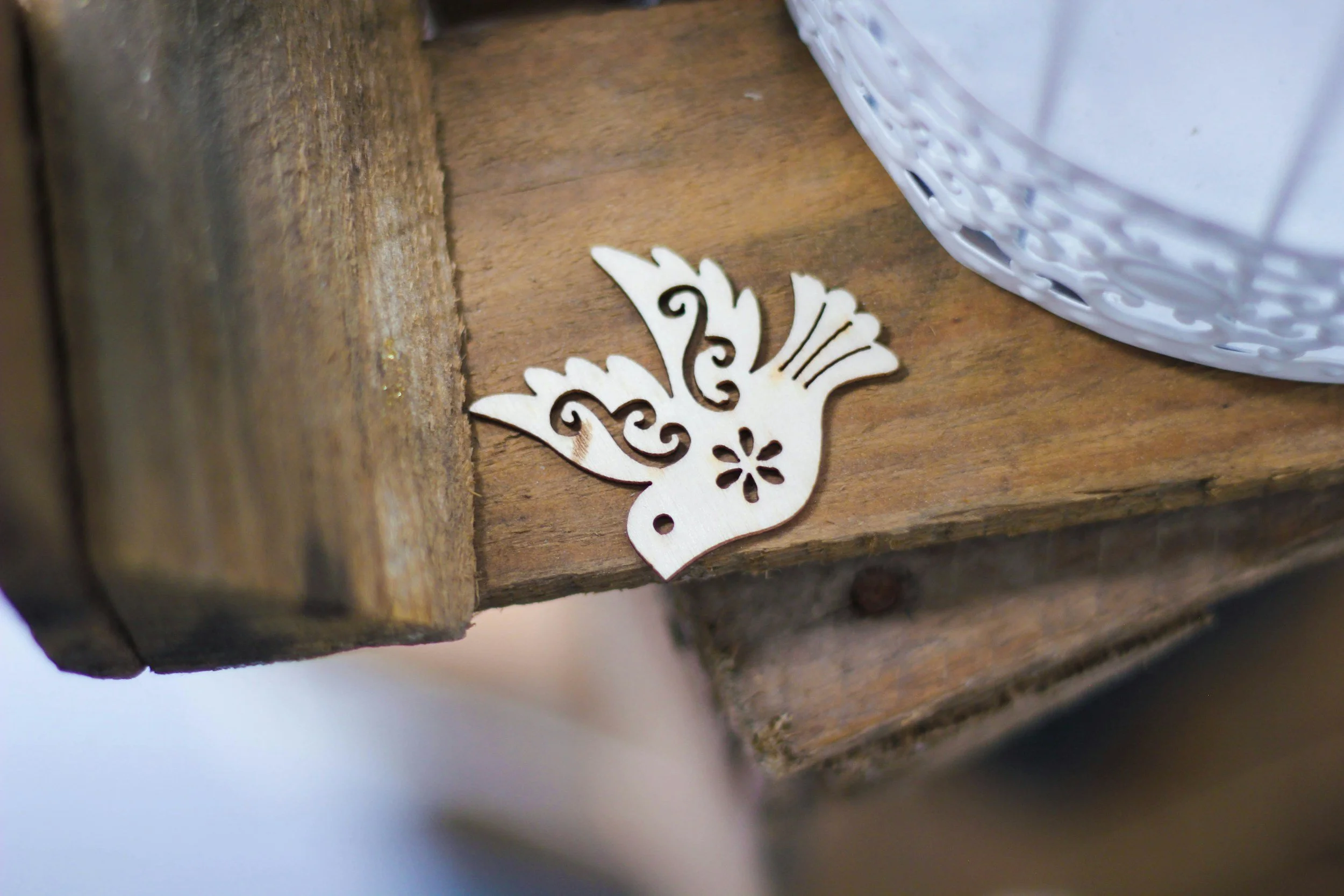 A decorative wooden bird ornament with intricate cut-out design lying on a wooden surface next to a white wicker basket.