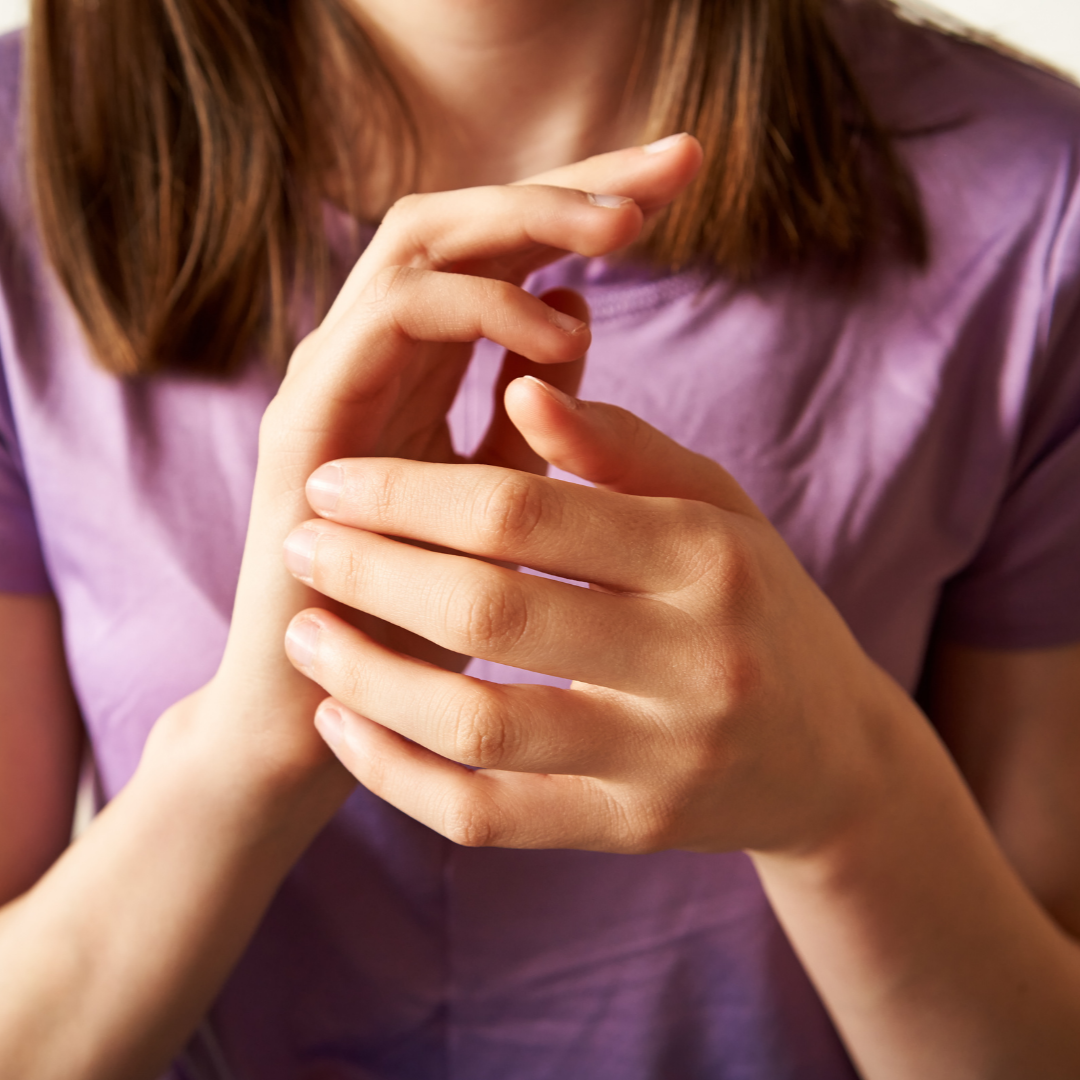 Close-up of a person with red hair wearing a purple shirt, hands gently clasped.
