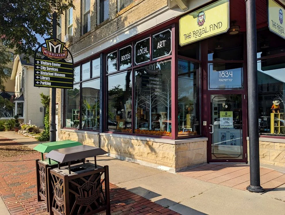 Street view of a downtown building Middleton where The Regal Find is located. The shop has a storefront with large windows and a maroon door, displaying items inside. A street lamp, a trash bin, and a sidewalk are in front.