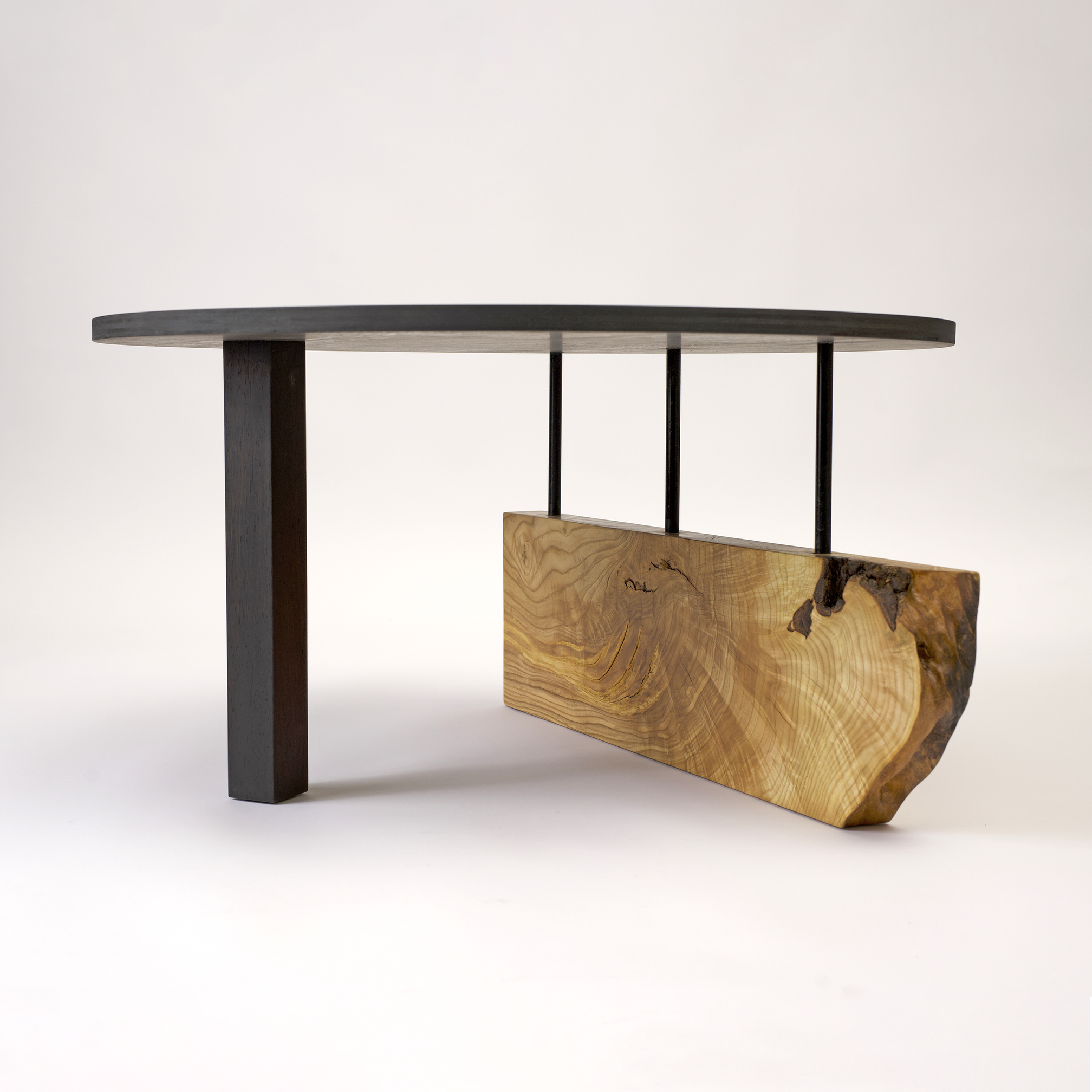 Modern table with a dark wood oval top, black metal supports, and a thick natural wood base, made by Forma Custom Furniture.