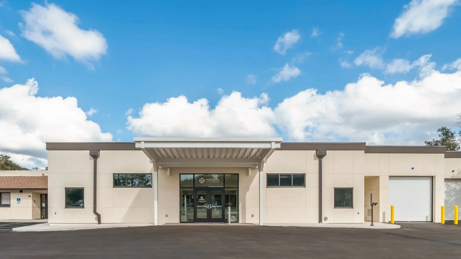 Front view of a building with a white exterior and glass entrance doors, labeled Meridian Healthcare, under a blue sky with clouds.