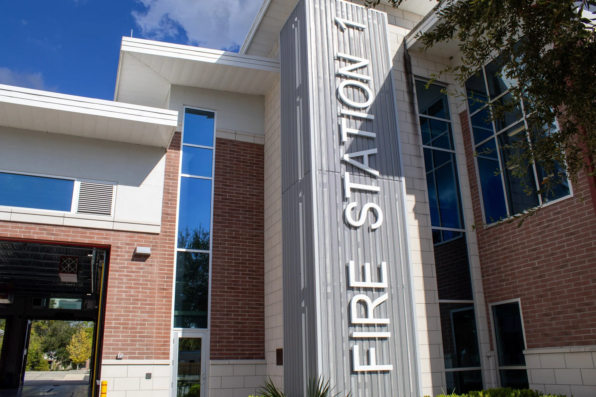 The exterior of a modern educational or institutional building with a brick and glass facade, large vertical sign reading 'LARETA STATION', and some greenery in front.
