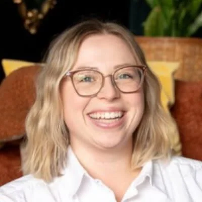 Kelsey Hunter is a white woman with wavy shoulder length blonde hair and large glasses