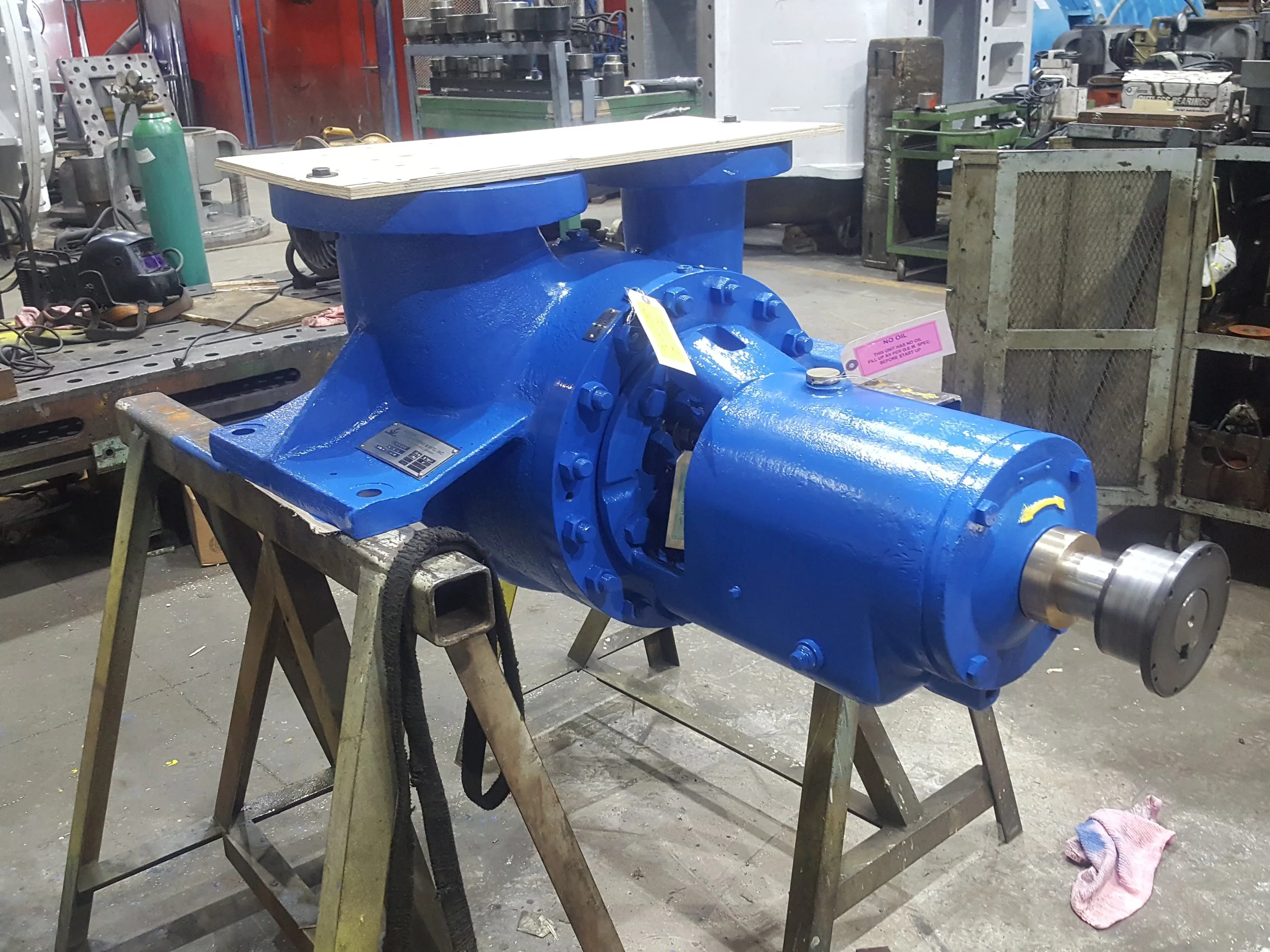 A large, industrial, blue-painted pump or motor on a wooden table in a workshop or factory setting.