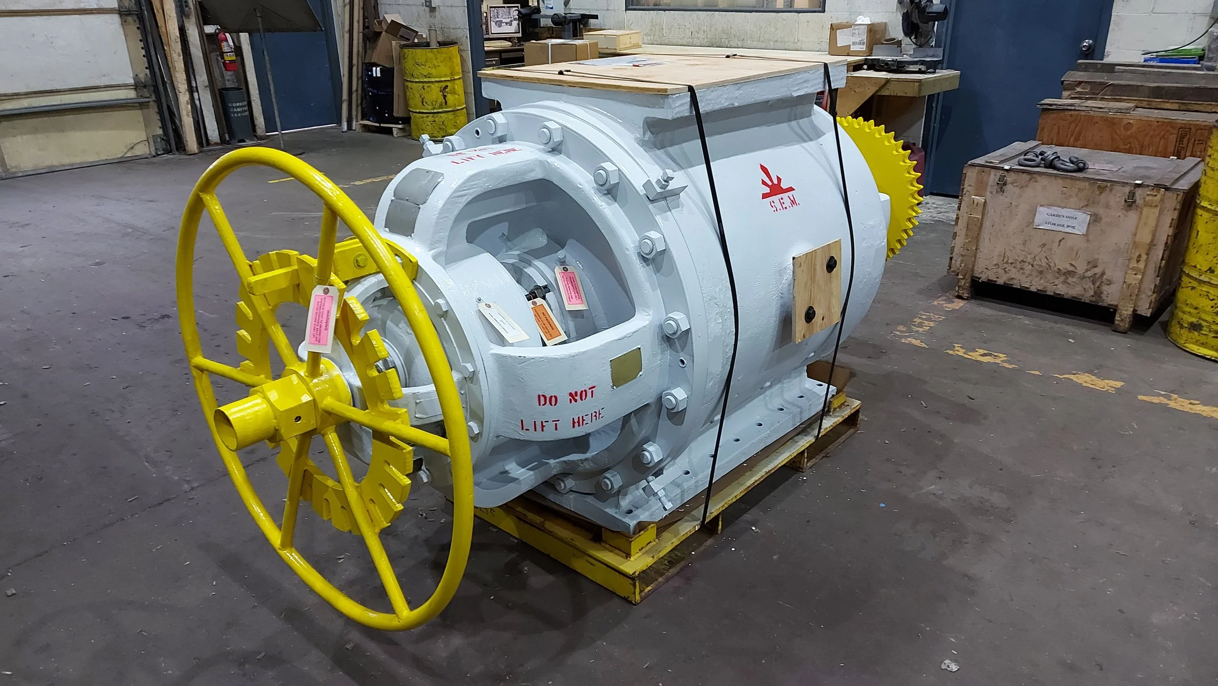 Sunrise Engineering - Large industrial machine with a yellow wheel and white body, sitting on a wooden pallet in a workshop. There are boxes and tools around.