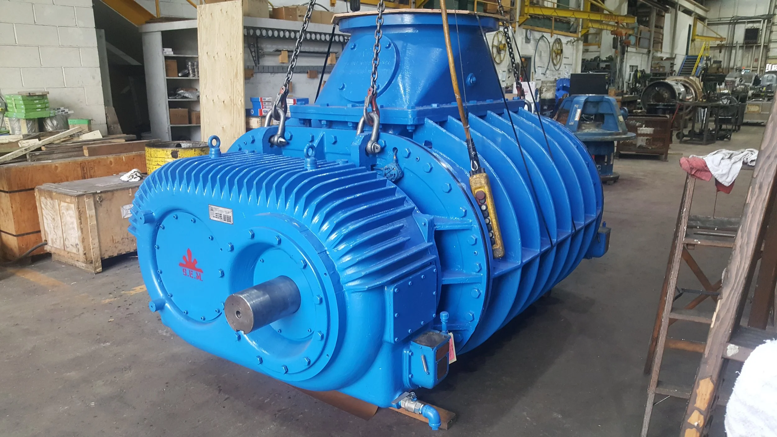 Sunrise Engineering - blue industrial machine with fins and a cylindrical shape inside a factory or workshop, surrounded by workbenches, tools, and equipment.