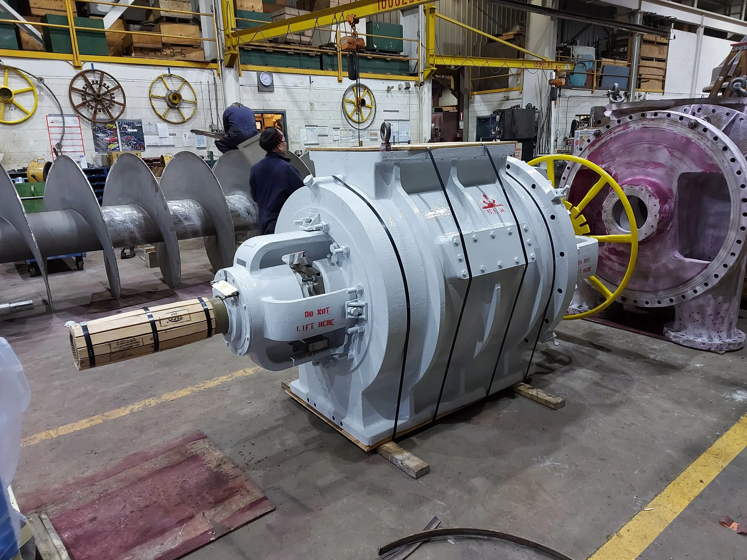 Sunrise Engineering - Large industrial machinery being assembled in a factory, with workers present, and various mechanical parts on the walls and floor.