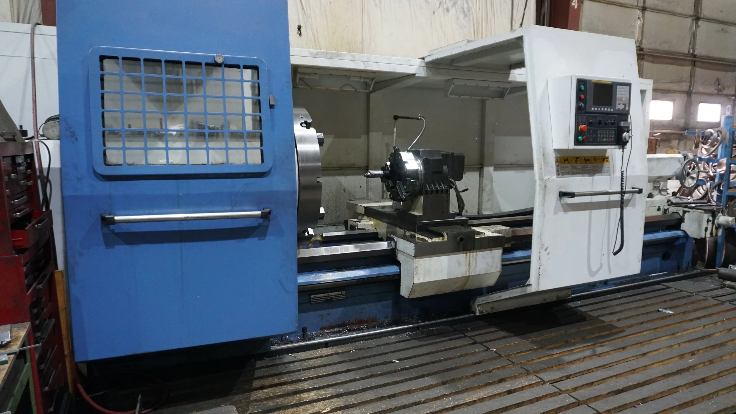 Sunrise Engineering - Industrial lathe machine in a workshop, with a blue and white color scheme, surrounded by workshop tools and environment.