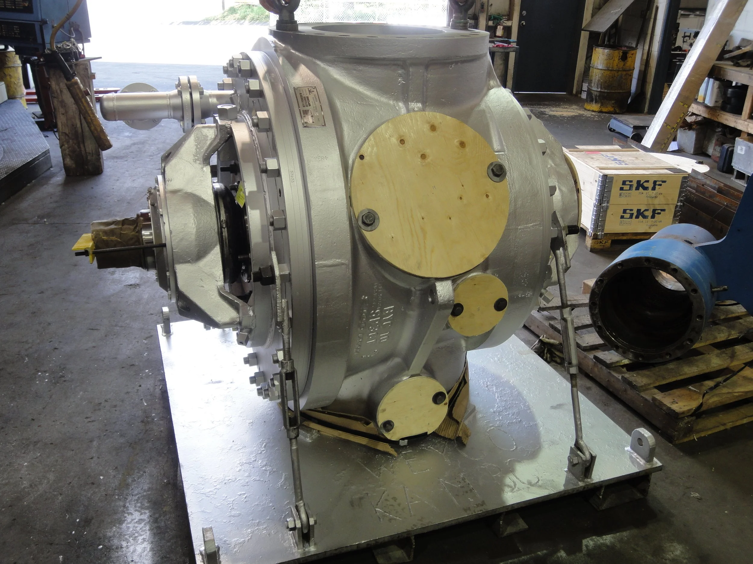 Sunrise Engineering - Large industrial mechanical component with metallic and yellow parts, on a warehouse floor with pallets and boxes in the background.