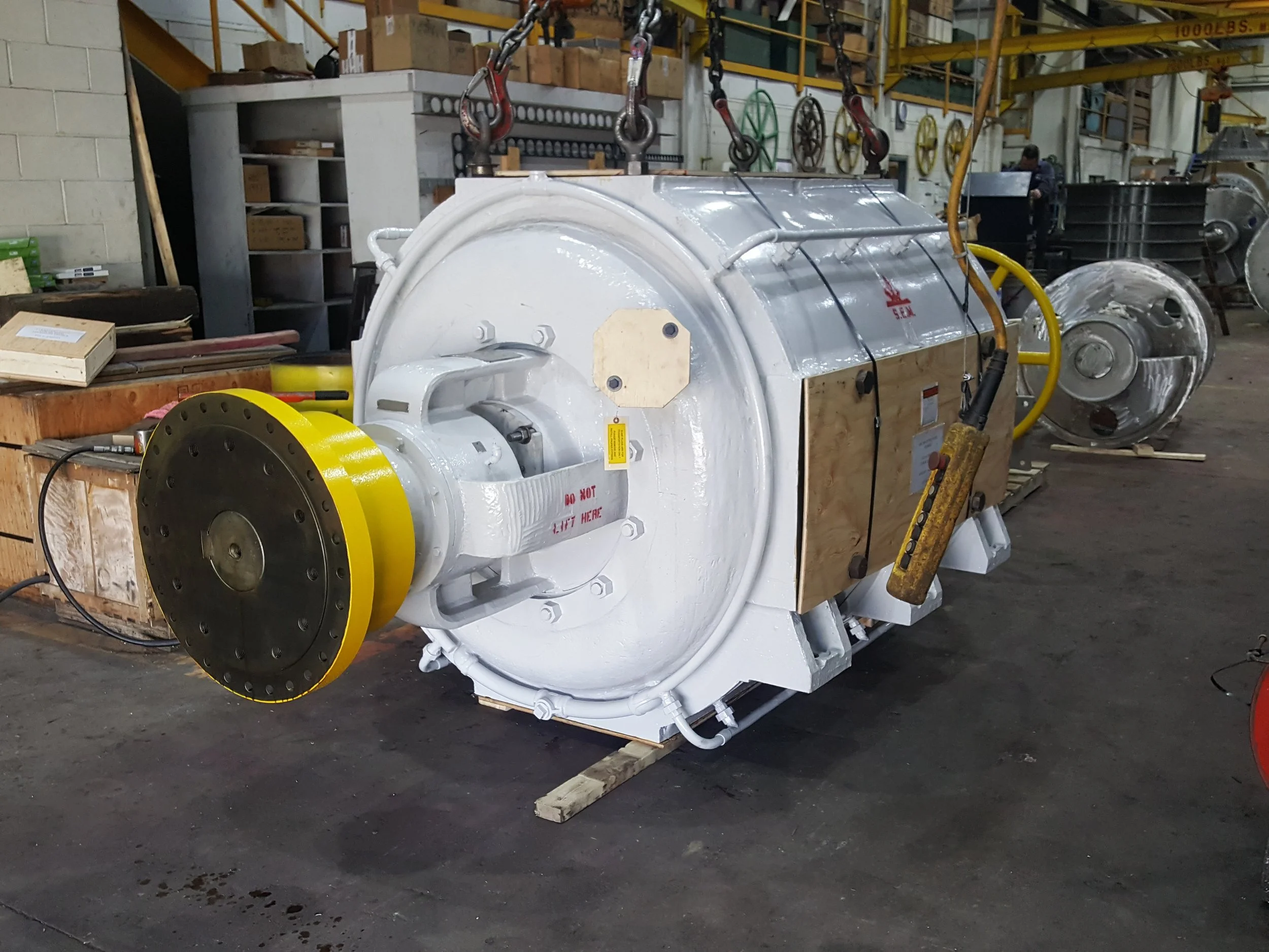 Sunrise Engineering -  industrial cylindrical machine, painted white with yellow accents, resting on wooden pallets in a manufacturing warehouse.