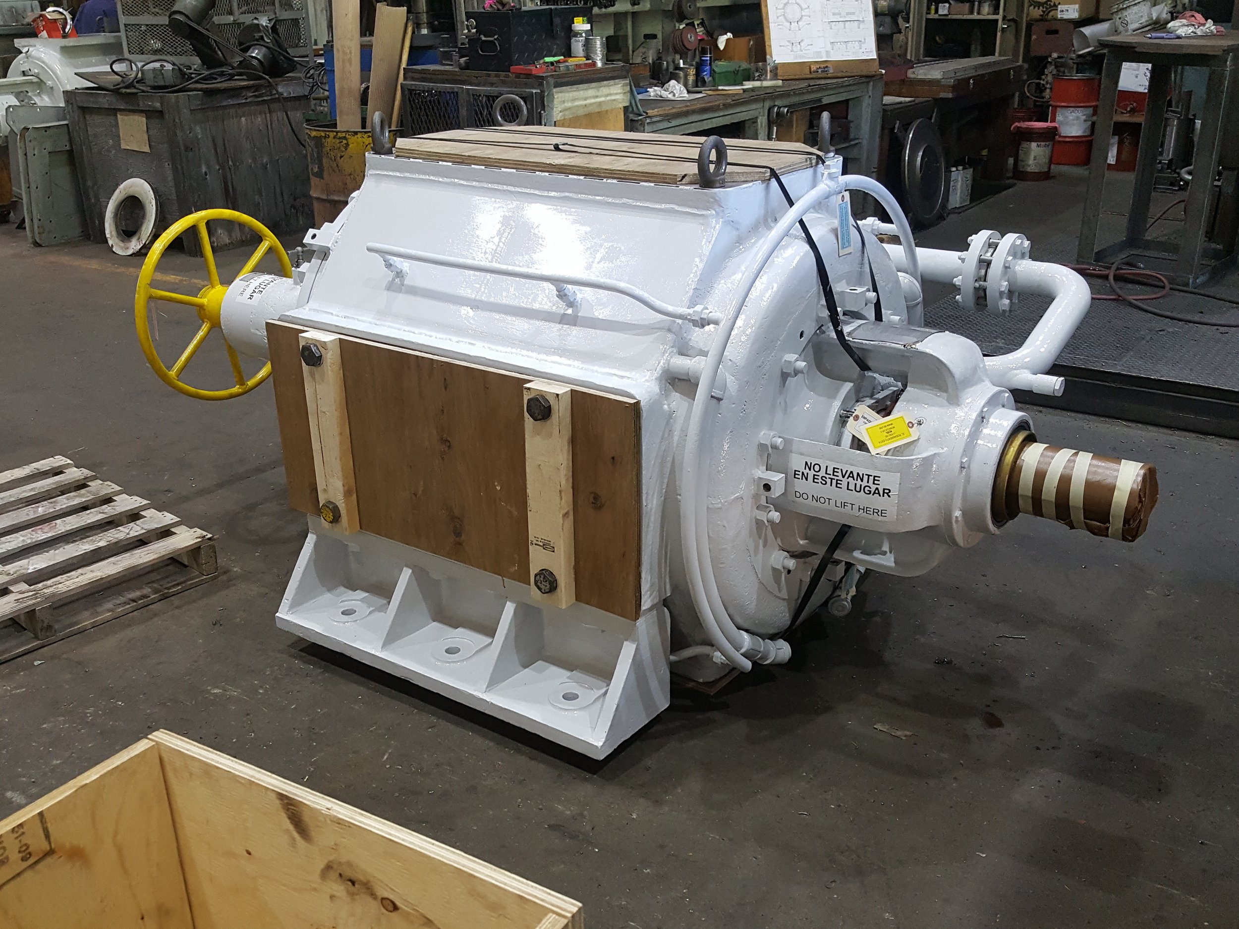Sunrise Engineering - Large mechanical device with white painted surface, yellow hand wheel, and wooden panels attached, situated in an industrial workshop.