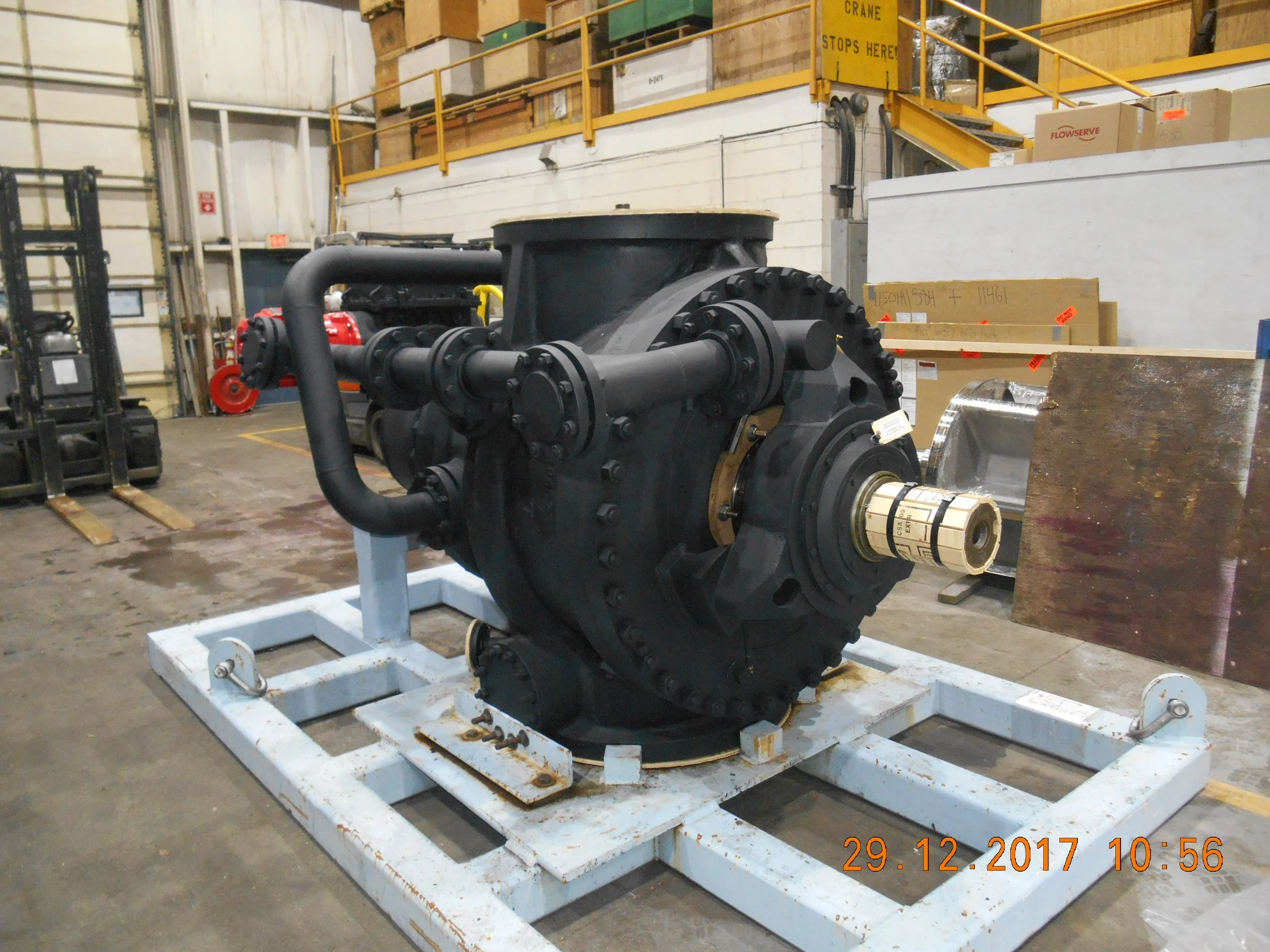 Sunrise Engineering - Large industrial machine with black casing and pipes, mounted on a white metal frame, inside a warehouse with shelving and boxes in the background.