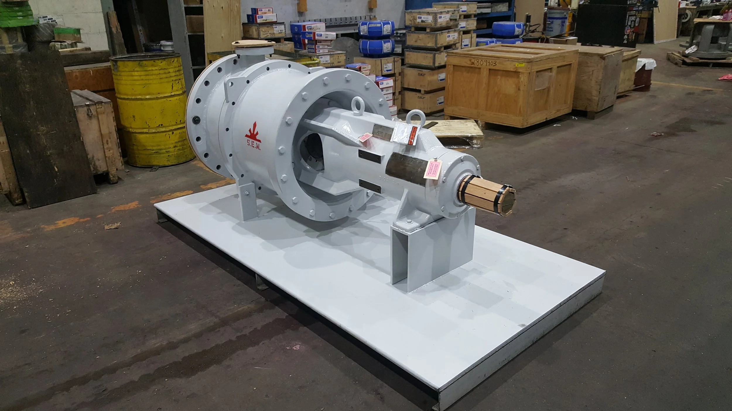 Sunrise Engineering -  industrial valve or pump component painted white, mounted on a metal base inside a warehouse, with boxes and crates in the background.