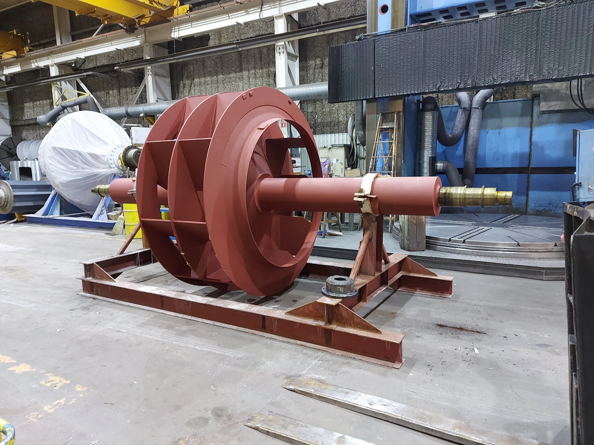 Large industrial equipment part with a cylindrical shaft mounted on a metal frame inside a factory or workshop.