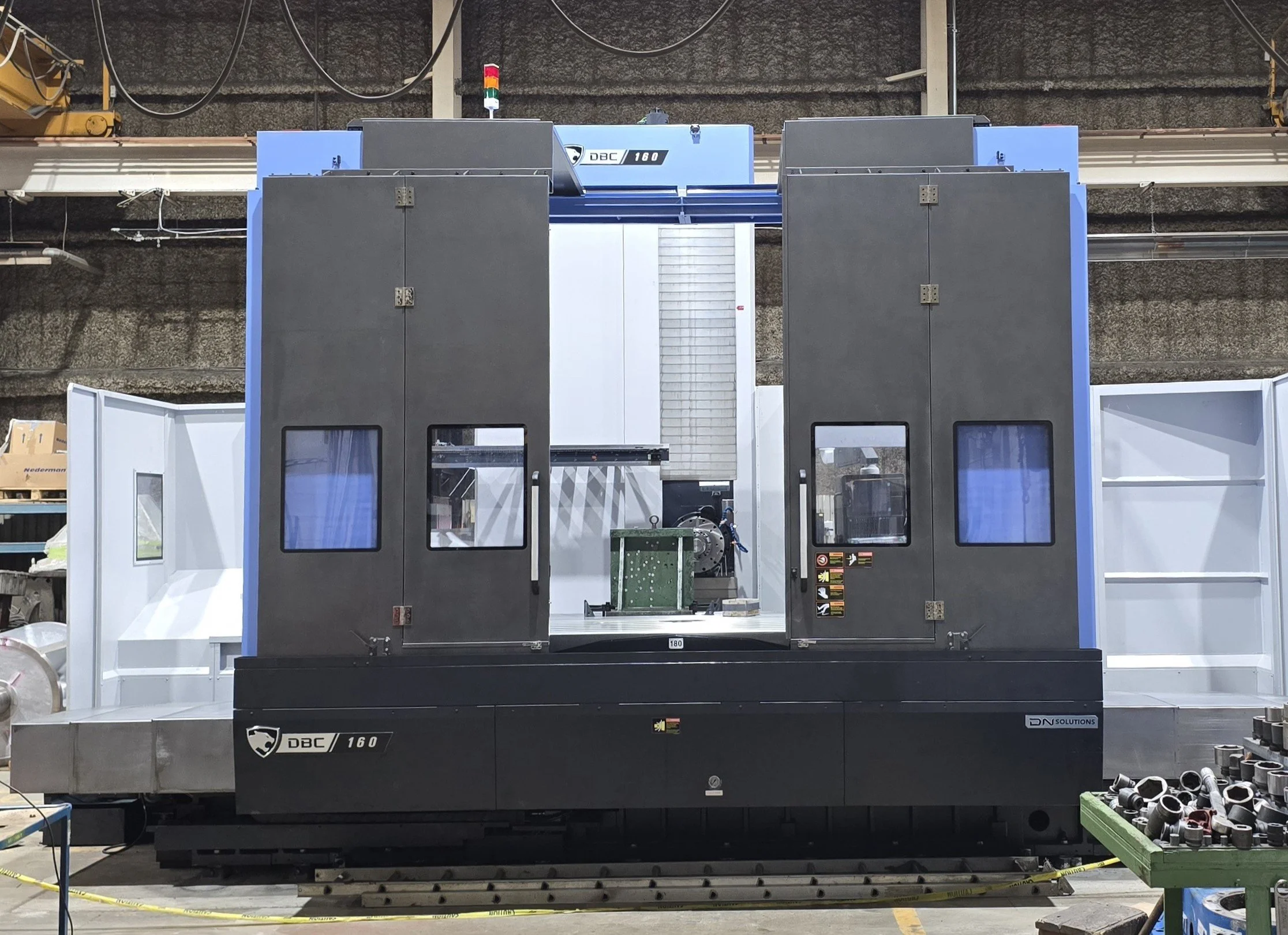 Sunrise Engineering - Industrial CNC machine in a manufacturing setting with black and blue panels, control panels, and metal components nearby.