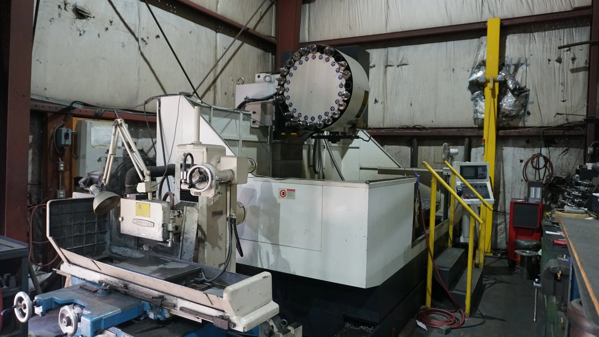 Sunrise Engineering - Industrial machine with a large circular component, metal control panel, and various tools and equipment in a workshop.