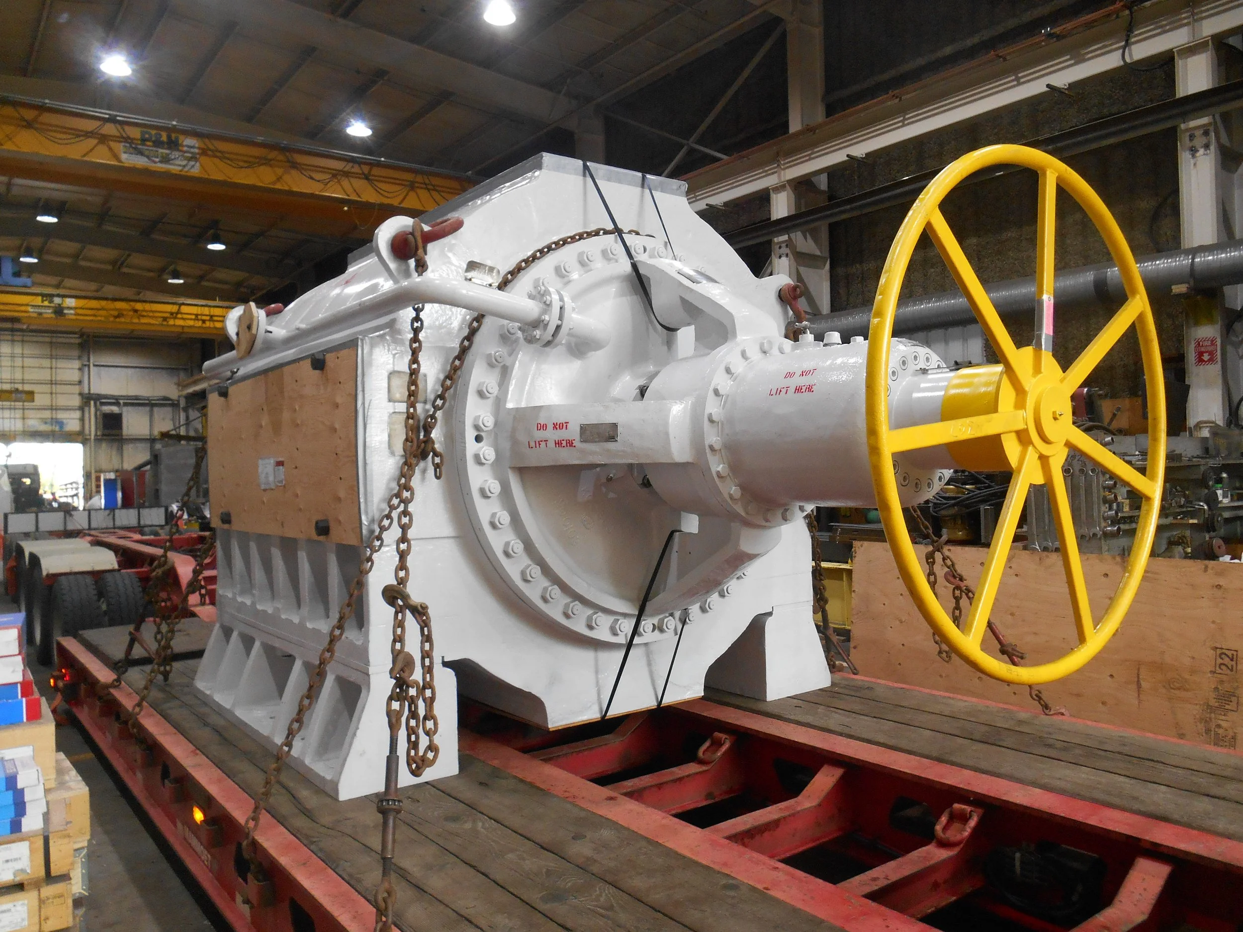 Large industrial machine with a yellow wheel, mounted on a flatbed in a warehouse.
