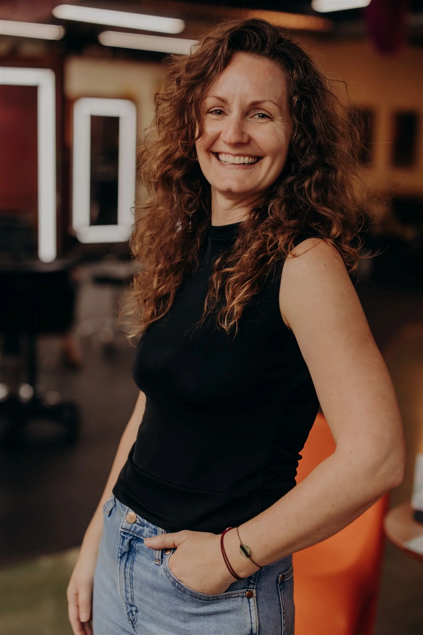 Portrait of a woman with curly brown hair, smiling, wearing a red tie-dye shirt against a blue background.