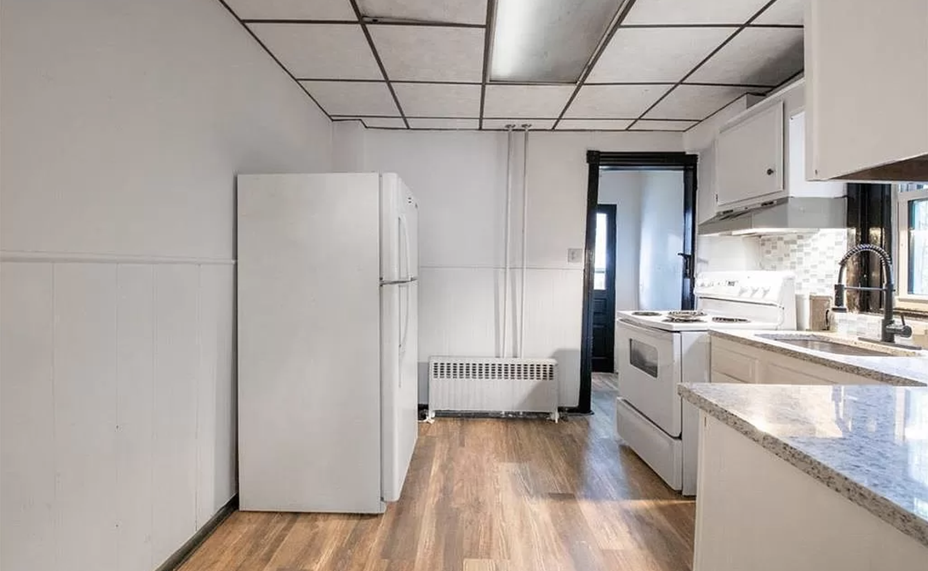 Empty kitchen with white cabinets, white stove and fridge, granite countertops, hardwood floor, black window frame, and a black door leading outside.
