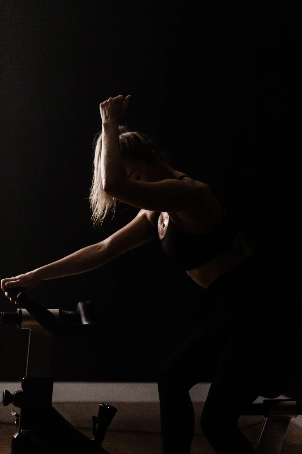 A white woman with blonde hair and  fist n the air on a spin bike