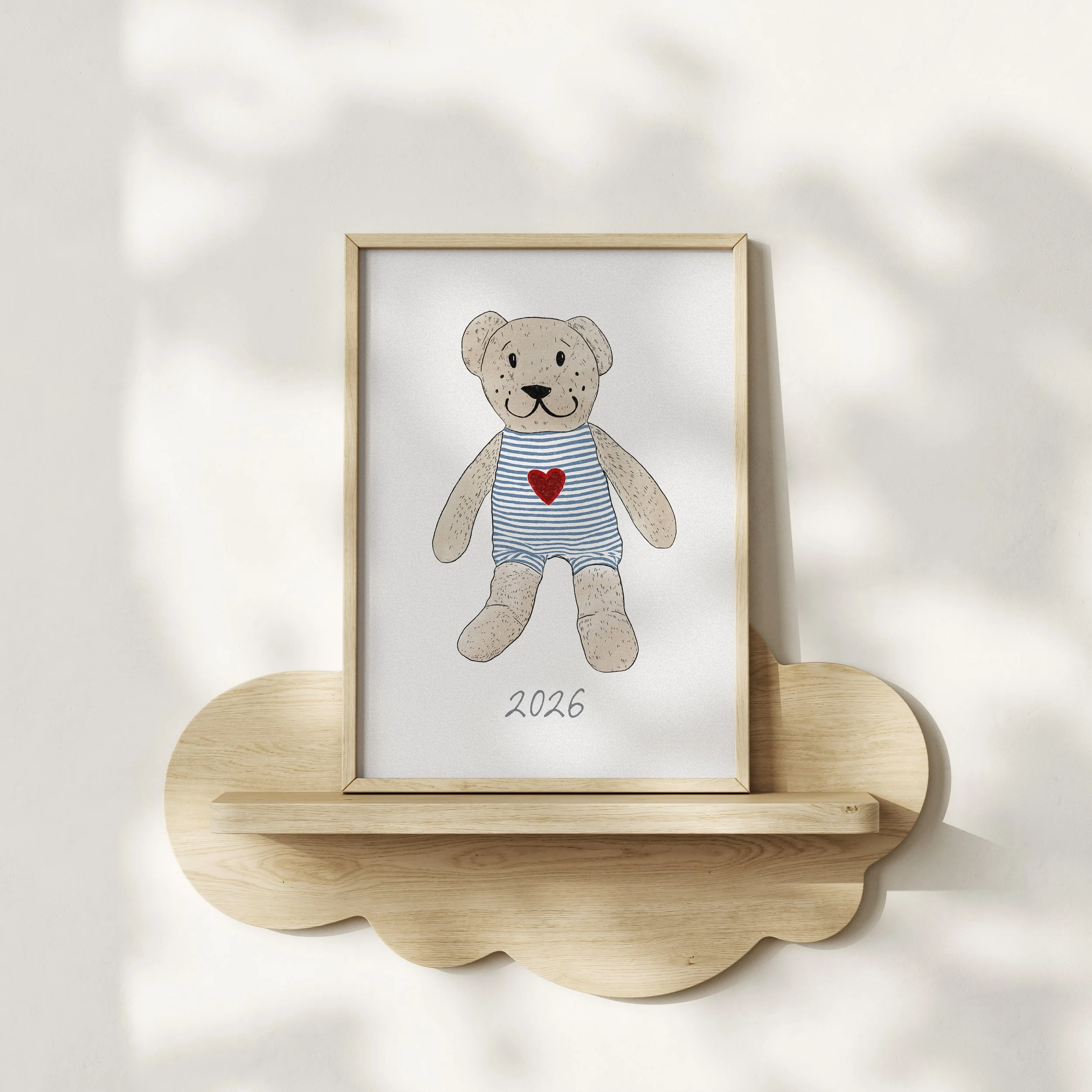 A framed drawing of a bear wearing a striped shirt with a red heart on its chest, placed on a wooden standing holder against a plain wall.