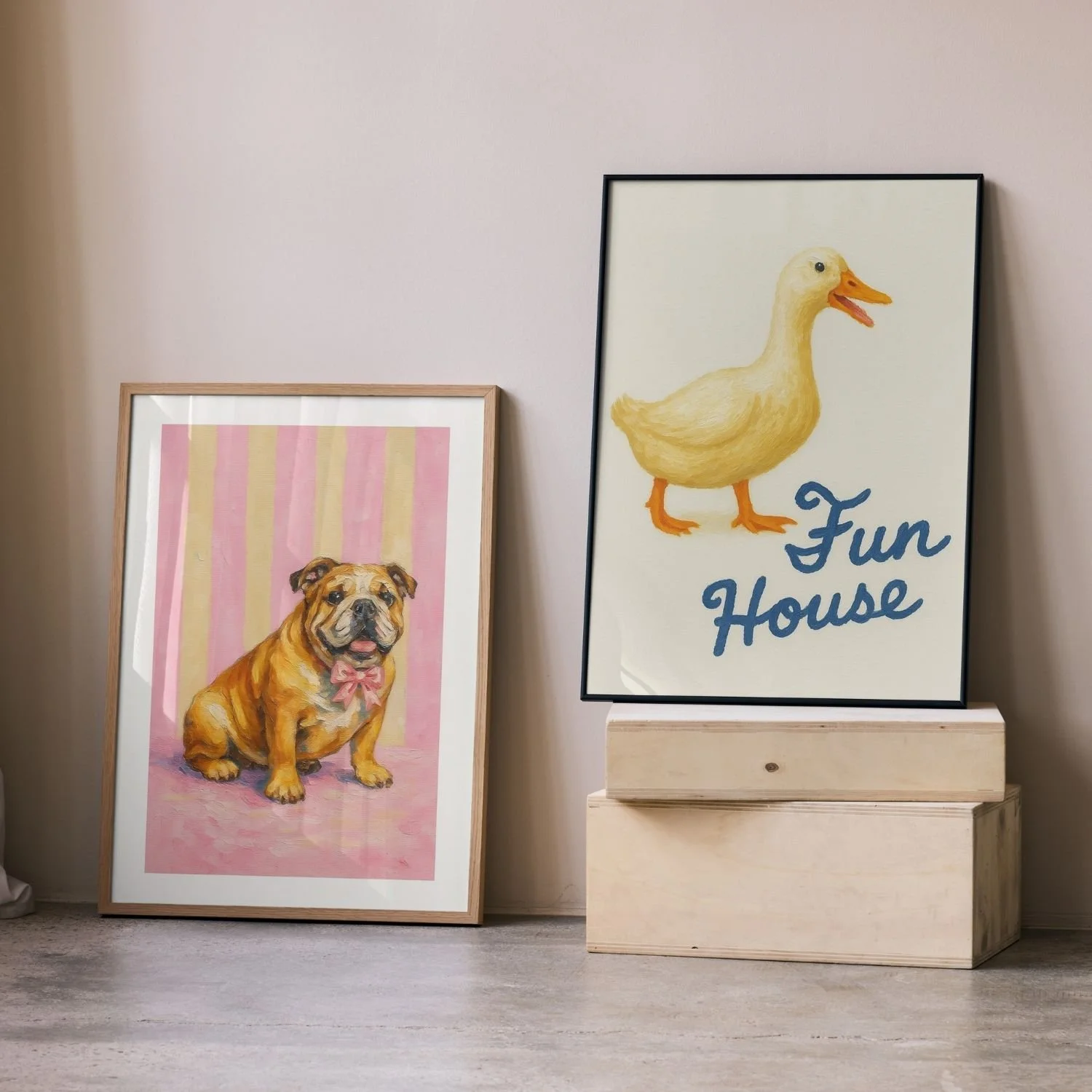 Two framed artworks leaning against a wall: one features a cartoon-style bulldog with a pink bow on a pink and yellow striped background, and the other features a duck with the text "Fun House" on a white background.