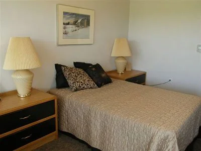 A bedroom with a bed, two nightstands with lamps, and framed artwork on the wall.