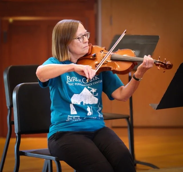 A woman playing a violin during a practice session or performance in a music room.