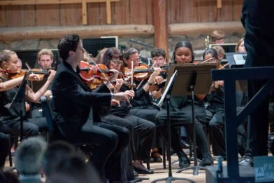 Orchestra of young musicians playing violins during a performance in a wooden venue.