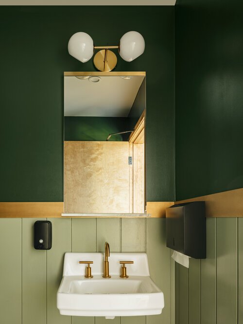  Modern, green bathroom at Greenwood Brewing with gold finishes. 
