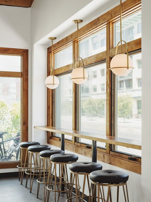  Cushioned bar stools line up against a natural wood bar top looking out of Roosevelt Row of Phoenix at Greenwood Brewing.  