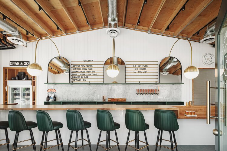  Green bar stools with backs, exposed ceilings, natural wood bar, arc pendant lights, Carrera marble backsplash and custom signage at Greenwood Brewing in Phoenix.  